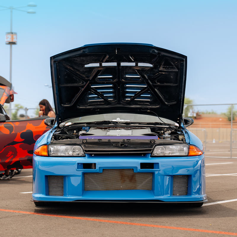 Blue Nissan Skyline EV conversion with open hood in a parking lot with another colorful car in the background.