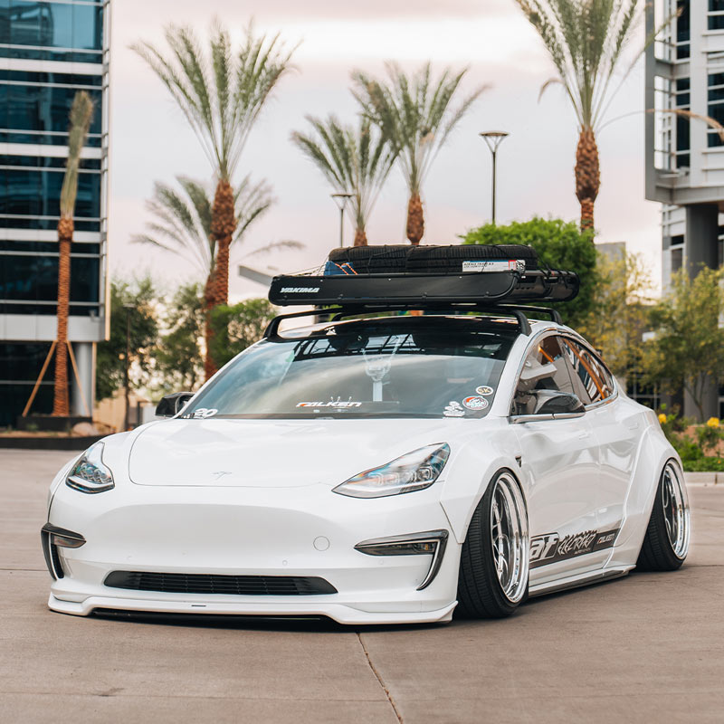 White Tesla custom EV parked on a street with trees and a stop sign in the background