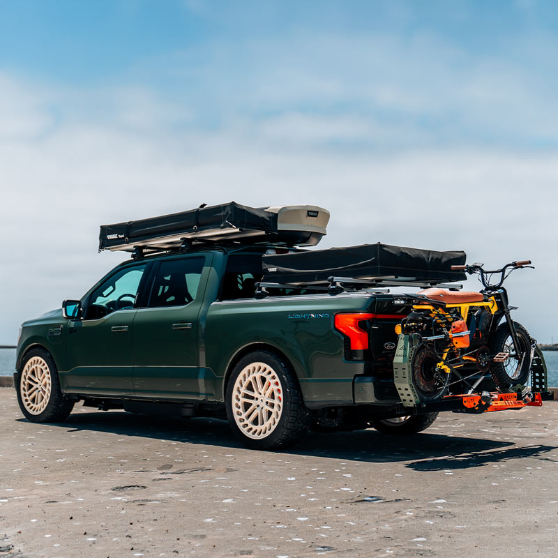 Green offroad pickup truck with roof racks and a bicycle on a beach