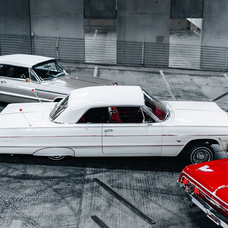 Vintage lowrider cars parked in a concrete lot.