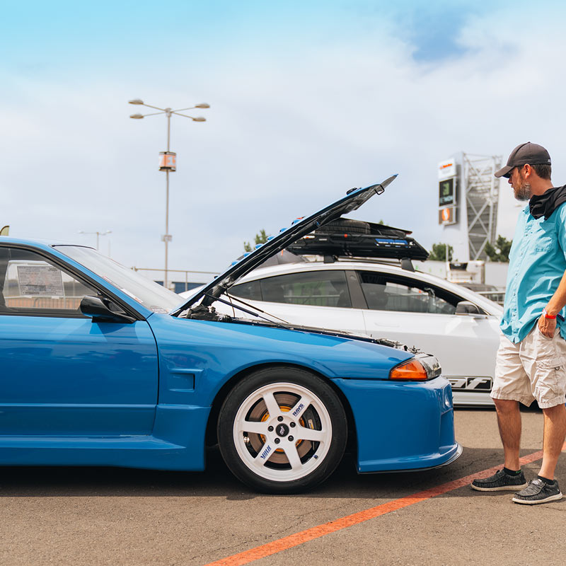 Blue custom JDM car with open hood in a parking lot, person standing nearby